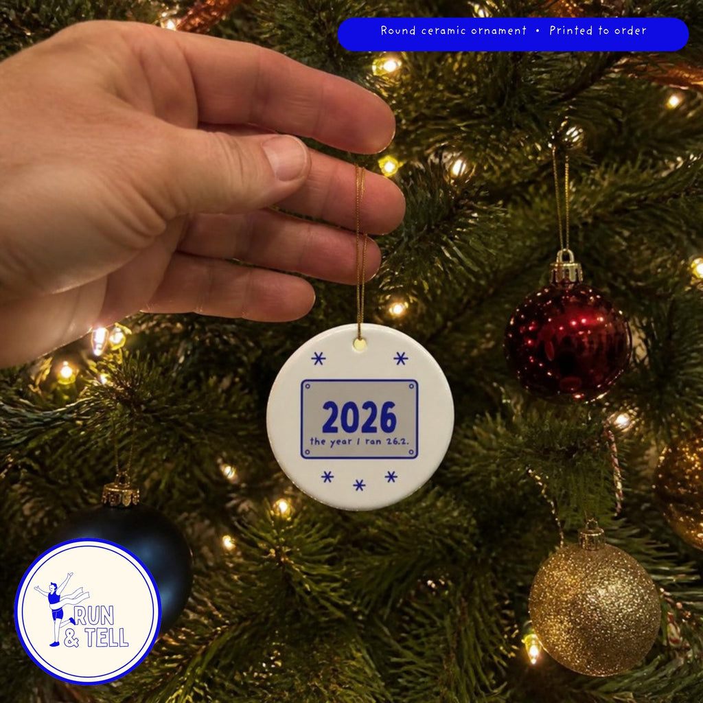 2026: The Year I Ran 26.2 ornament hanging on a Christmas tree among glass baubles