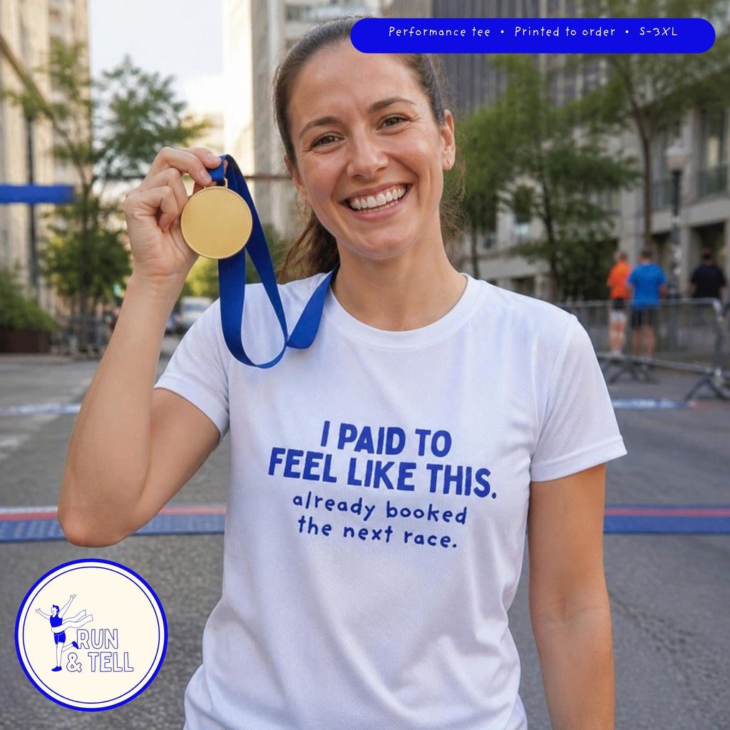 Runner holding up a finisher medal after a race, wearing the white I Paid to Feel Like This performance running tee